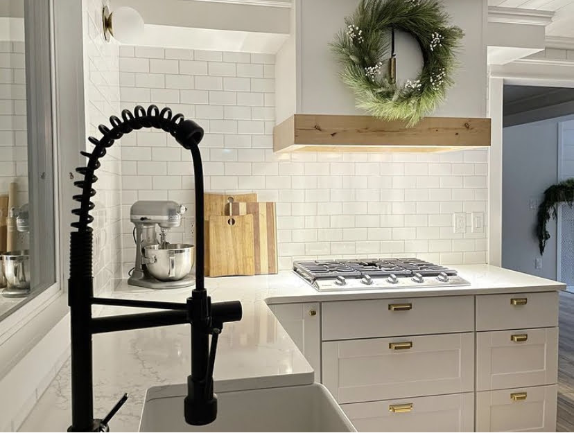 black faucet in kitchen with wreath and white countertops and tile backsplash