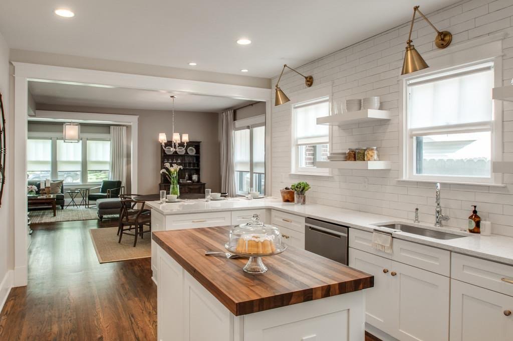butcher block island with cake in kitchen with white countertops, white cabinets and white tile backsplash