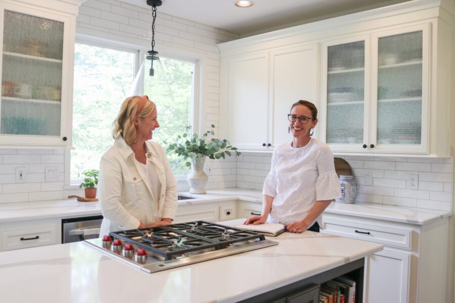 two women laughing at a kitchen island with a cooktop