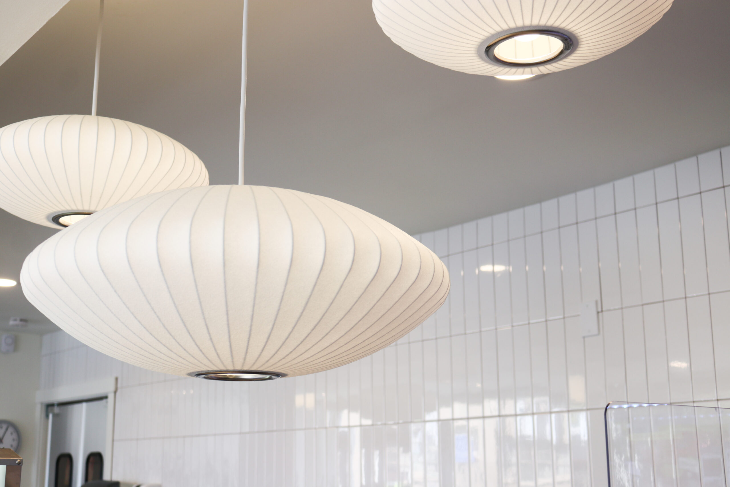 white pendant lights hanging from the ceiling with white tiled walls