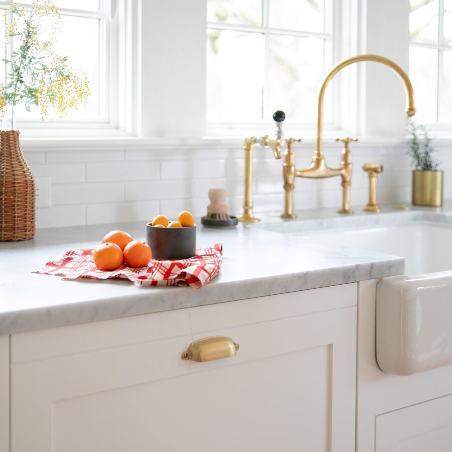 oranges on white countertops with brass faucet